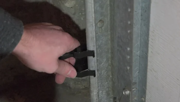 Attach the garage door sensor laser holder brackets to the garage door using pressure; no bolts needed. Ensure the prongs don't extend beyond the track.