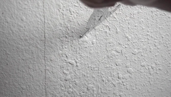 Carefully remove the excess drywall using a knife, creating a clean, recessed area around the nail or screw.