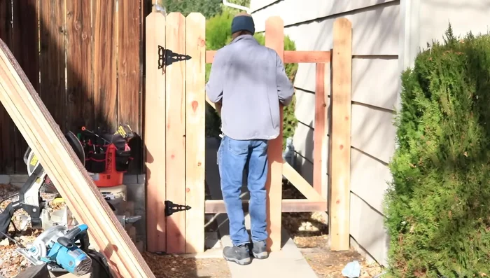 Hang the gate, using shims if needed to adjust height. Ensure proper alignment with the fence posts, leaving a small gap if necessary. Attach hinges fully after verifying fit.