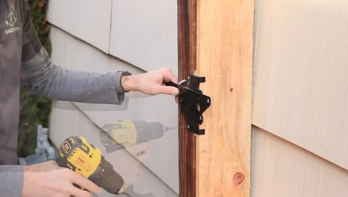 Mount the latch mechanism and strike plate, pre-drilling and using supplied fasteners. Ensure the strike plate is secured to the 2x4 support.