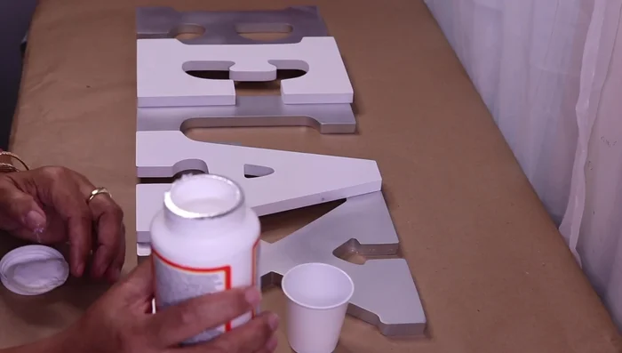 Decorate the letters using crushed glass and Mod Podge. Apply Mod Podge, add crushed glass, let it sit for 10 minutes, shake off excess, and fill in gaps with more glass and Mod Podge. Add glitter for extra sparkle.