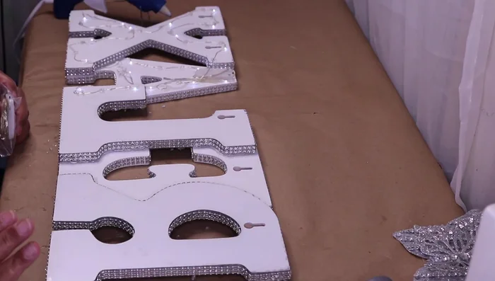 Add string lights to the back of the letters. Secure the battery pack with hot glue and carefully wire the lights around the outline of each letter, hiding excess wire.