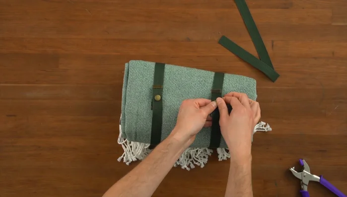 Add a handle to the blanket using the longer strap and brass details, securing it with screws.