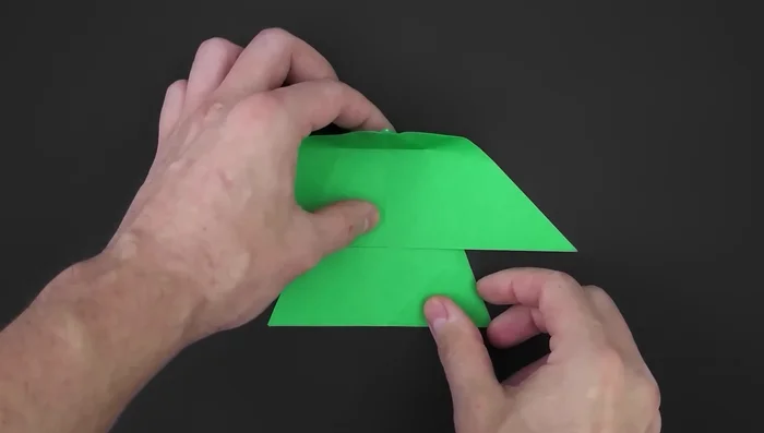 Bring the top layer behind the middle part, aligning the diagonal edge with a specific point. Flatten and reinforce on the other side. Repeat on the other side.