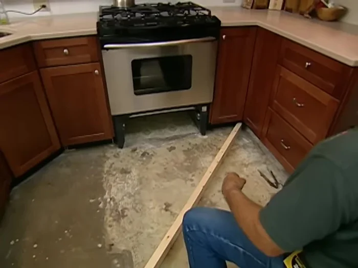 Cut and install the first rail: Cut the rail along the scribed line. Position the rail on the floor and check for level. Attach it securely using construction adhesive and screws.