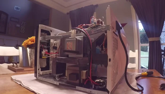 Carefully remove the top cover of the microwave to access the internal components. Be cautious of the high-voltage capacitor; if unsure, discharge it safely using an insulated screwdriver.