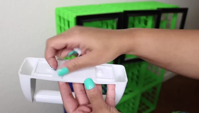 Attach paper holder: Remove the lining from a Dollar Tree paper holder, add E6000, and press it against the crates. Use hooks for additional support to hang items like loofahs or brushes.