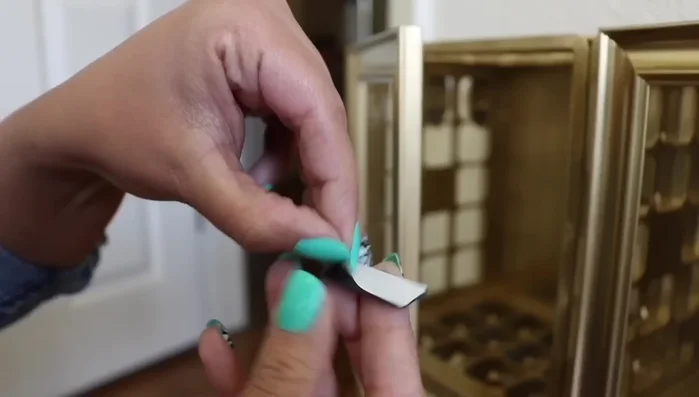 Attach magnetic strip: Remove the lining from a Dollar Tree magnetic strip, apply hot glue, and attach it to the bottom of the door. Add three metal thumb tacks for a secure closure.