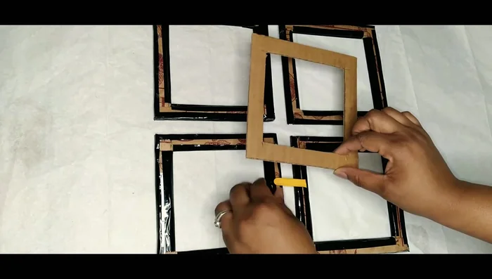 Use hot glue to attach the popsicle sticks between the squares, ensuring proper alignment and holding until the glue sets.