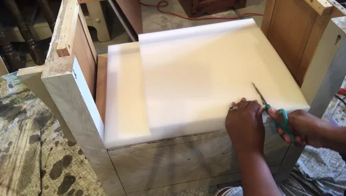 Attach fabric to the cushion, pulling taut and securing with nail trim.