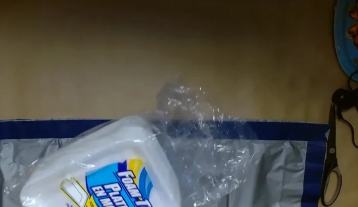 Add decorative elements: Cut and attach the foam trays to create a roof-like structure. Use painter's tape to secure the foam trays. Create a sign using the placemat and letters, attaching them with painter's tape.