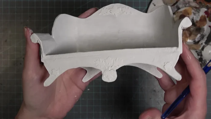 Paint the couch with a base coat of white acrylic paint, followed by a dry brush of gray for highlighting.