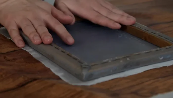Transfer to cloth sheet: Place the mold onto a cloth sheet. Carefully lift the deckle off the mold. Use a sponge (or alternative) to press out excess water.
