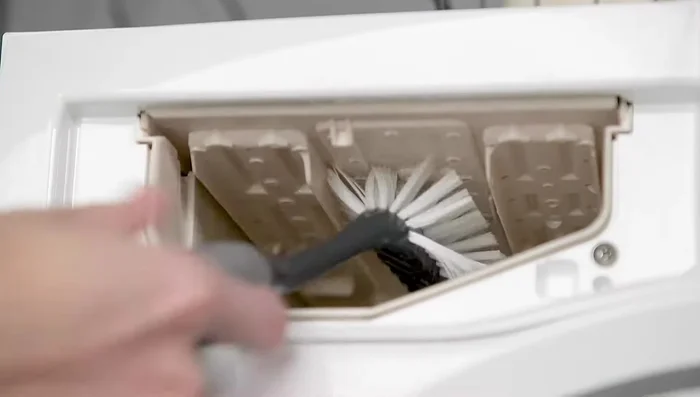 Clean the dispenser housing using warm water and a nylon brush, paying close attention to the top underside of the drawer opening where the shower holes are located.