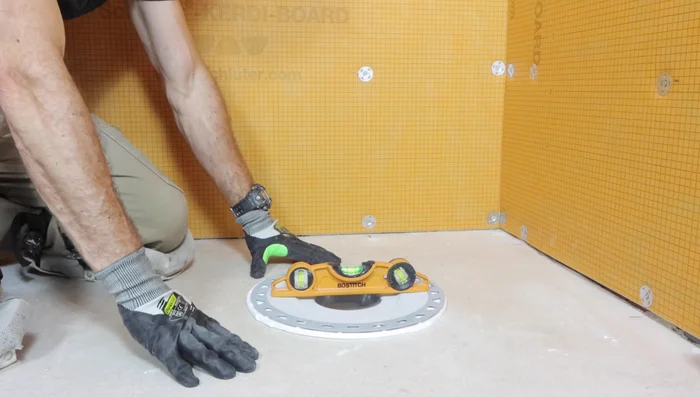 Apply thinset to the top and bottom of the halved foam insert and place it between the floor and the drain for support.