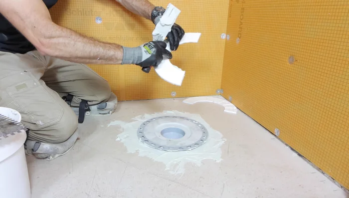 Apply thinset to the top and bottom of the halved foam insert and place it between the floor and the drain for support.