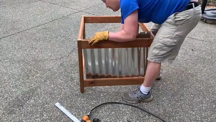 Cut corrugated metal to size using aviation snips. Attach the metal to the wood frame using brad nails and a brad nailer.