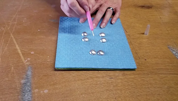 Punch holes in the centers of the aluminum pieces for beads; punch a hole in only one piece if making a charm.