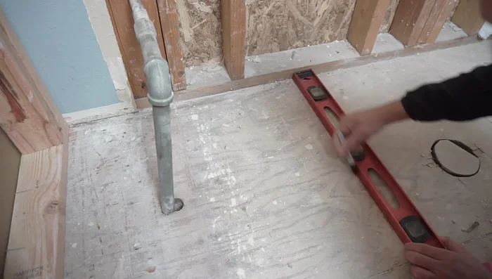 Locate the floor joists using a stud finder to determine the best placement for the new pipe route, ensuring it avoids structural compromises.