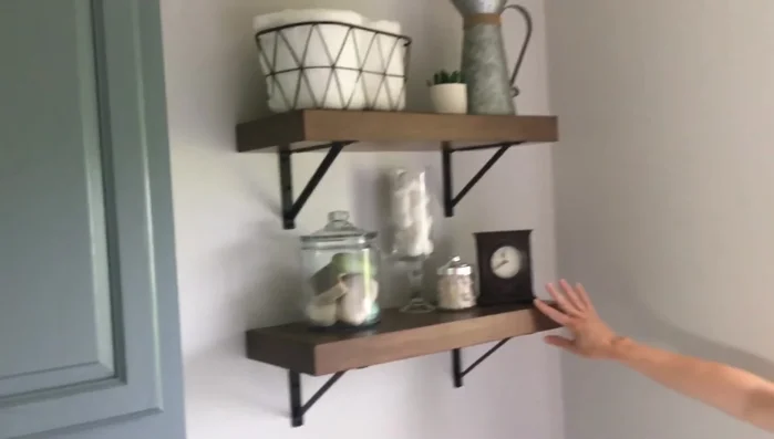 Shelving Installation: Add shelving above the toilet using simple kitchen shelves from a home improvement store and decorate with a mix of materials (metal, fabric, greenery, galvanized metal, glass) for a Farmhouse aesthetic.
