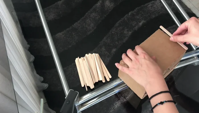 Apply hot glue to the top and bottom of a popsicle stick and attach it to the box. Repeat until the box is covered.