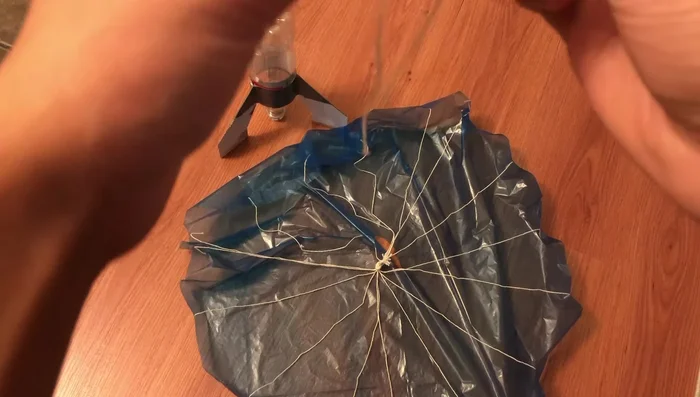 Cut a 30cm string, tie a knot in the middle. Attach one end of this string to the parachute knot, and the other end to the bottle top using a rubber band and hot glue.