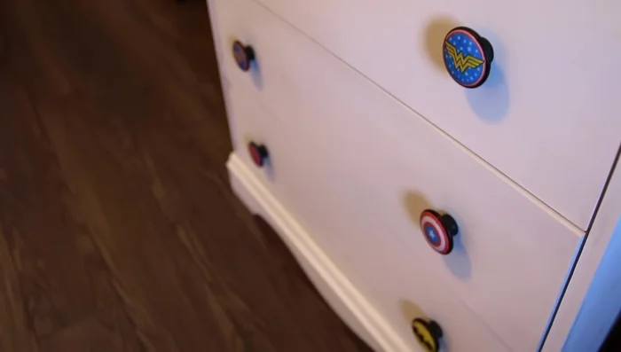 Customize dresser poles by painting inexpensive wood poles and adding superhero logos using Mod Podge.