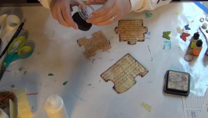 Distress the edges of the puzzle pieces using distress ink and mixed media ink. A makeup sponge can help with application.