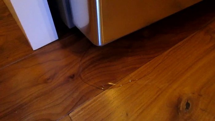 Identify the problem: Notice the puddle of water under the refrigerator.